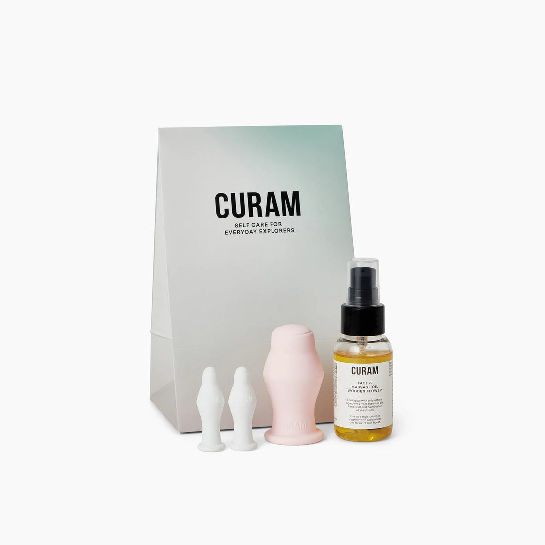 Curam Face Kit visat med minimalistisk förpackning, två vita silikonkoppar för ansiktskoppning, en rosa silikonkopp och en flaska Wooden Flower Face and Massage Oil med svart pumpdispenser.