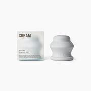 Curam Dynamic Cup i silikon i färgen soothing grey med strukturerad greppdetalj och präglad logotyp, visad upprätt bredvid sin varumärkta förpackning med mjuk gradientdesign.