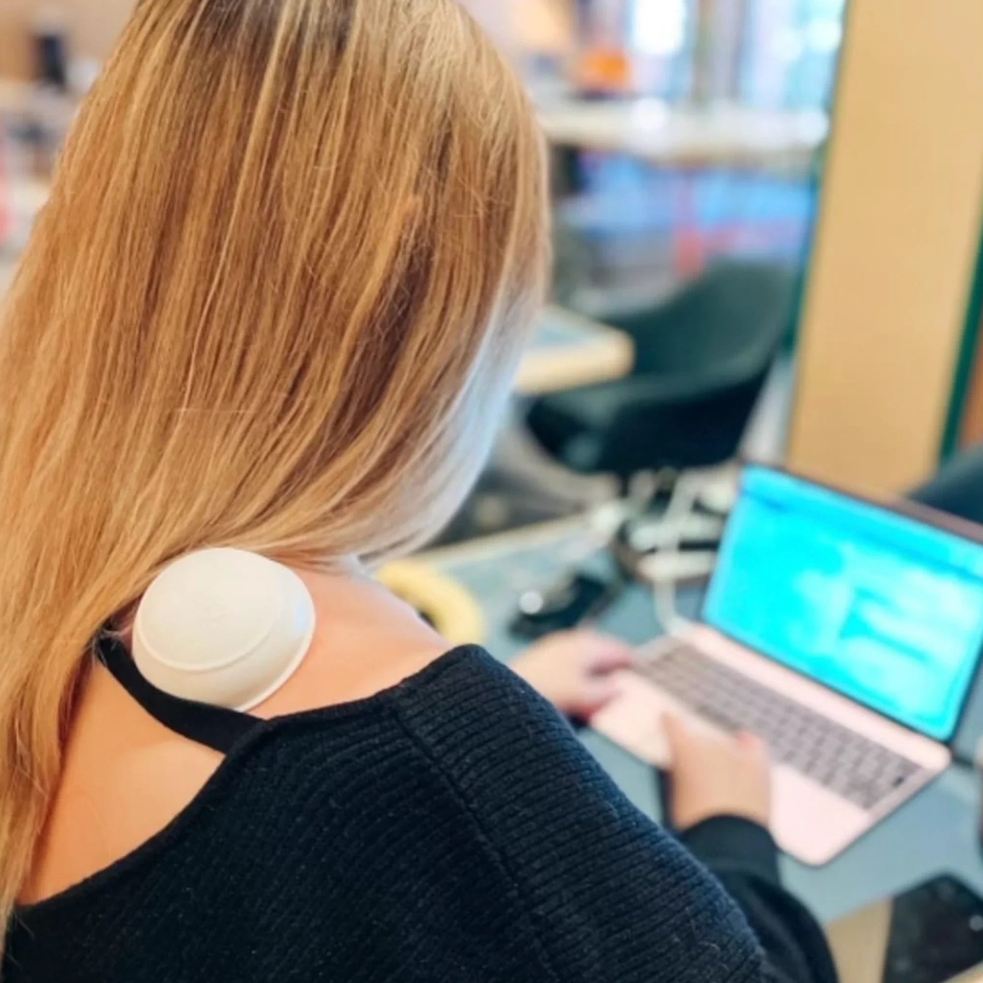Person arbetar vid laptop med en av Curams statiska massagekoppar på axeln