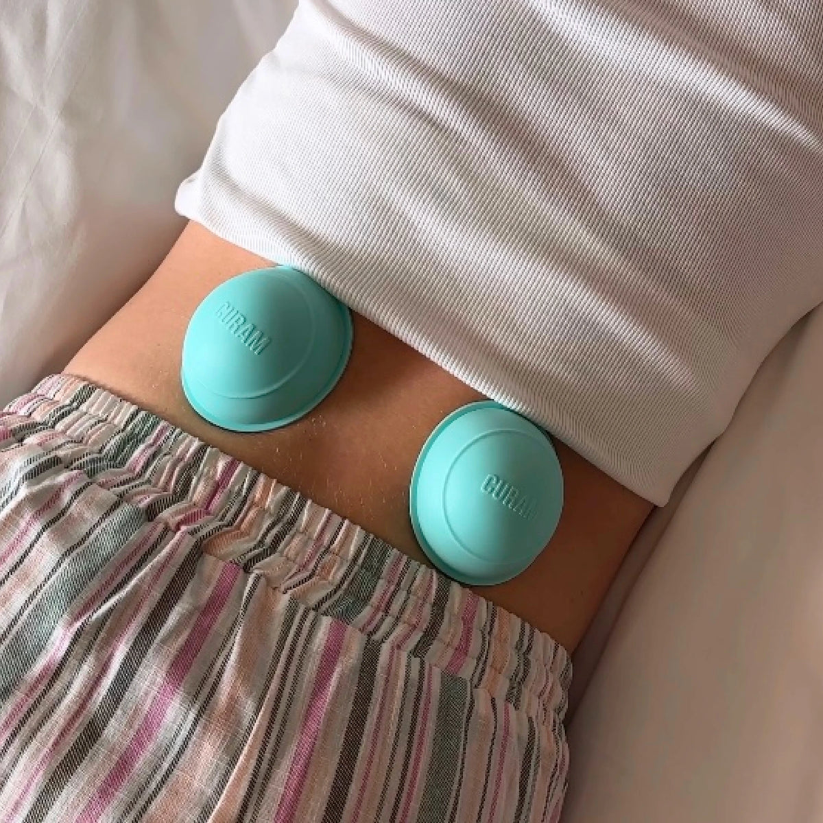 Two mint green Curam Static Cups placed on the lower back during a relaxation session, demonstrating hands-free static cupping therapy for muscle tension relief at home.